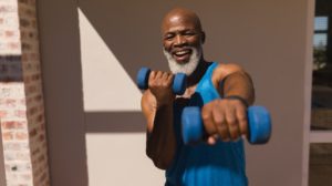 Front view of active senior African American man training arms with dumbbells in the backyard of home | featured