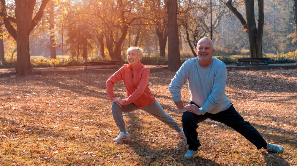 Senior man and woman exercise together outside in autumn park | featured