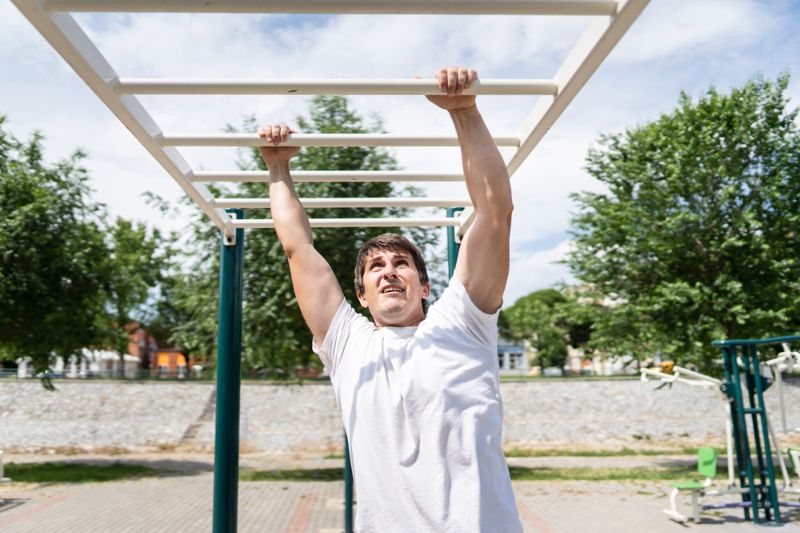 adult-caucasian-man-on-monkey-bars benefits of hanging from a bar