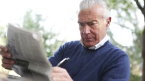 man in blue sweater holding pen and reading newspaper | Enlarged Prostate Causes, Symptoms, Treatment & Prevention | Featured