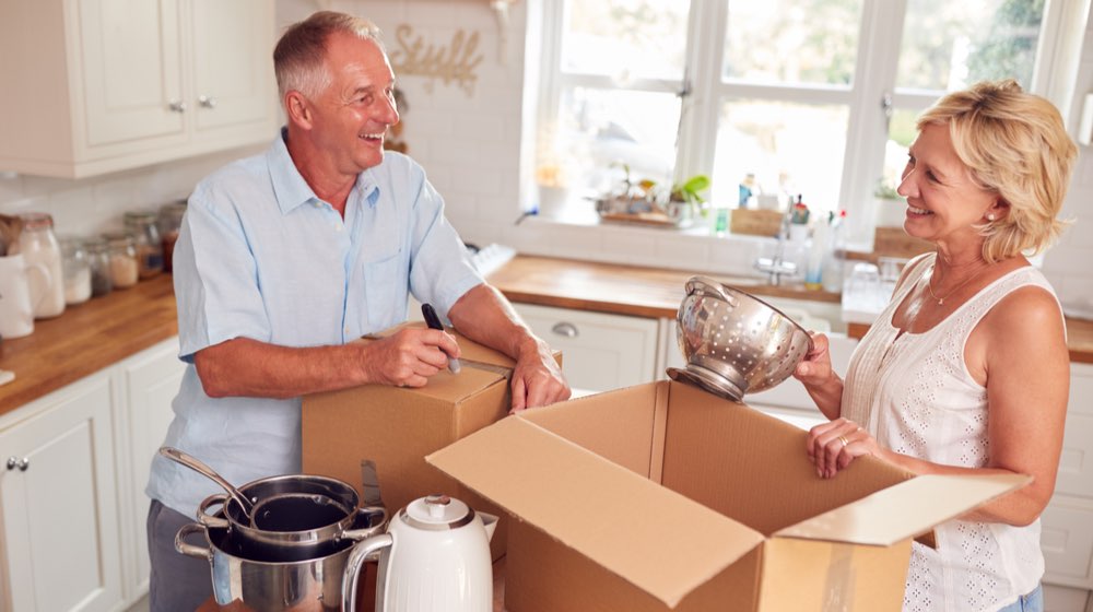 Senior Couple Downsizing In Retirement Packing And Labelling Boxes Ready For Move Into New Home | home downsizing