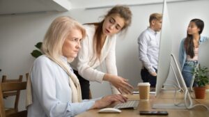 Young team leader correcting offended senior employee working on computer in office, scolding aged old worker |age discrimination | ageism in the workplace