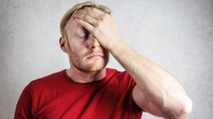 a man in red shirt covering his face | Peyronie's Disease FAQs | Featured