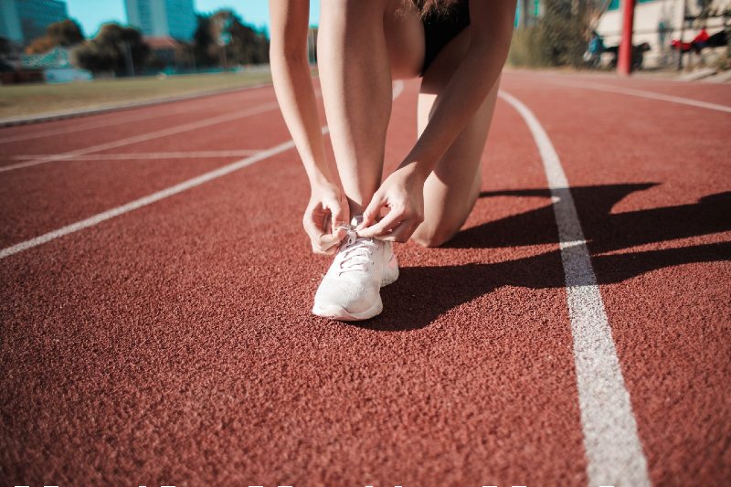 close up photo of woman tying her white sneakers on running track | running exercises to get faster