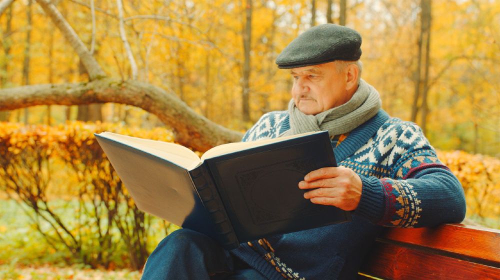 Old man is reading book alone on the bench in the autumn park-ss