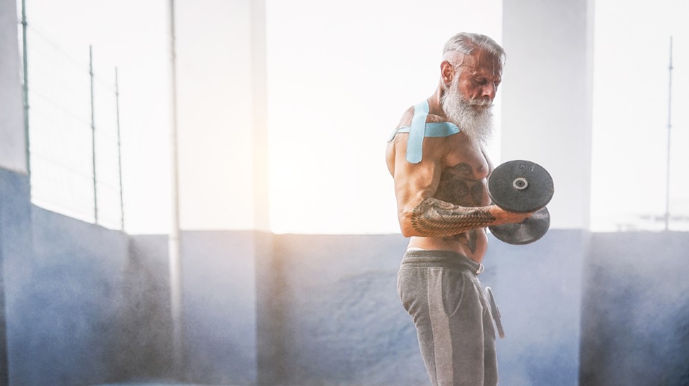 Senior fitness man doing biceps curl exercises inside old gym-ss