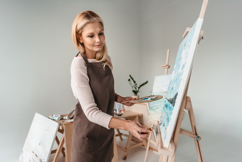 beautiful mature woman in apron painting on easel at art class | Amazing Benefits Of Turning 50