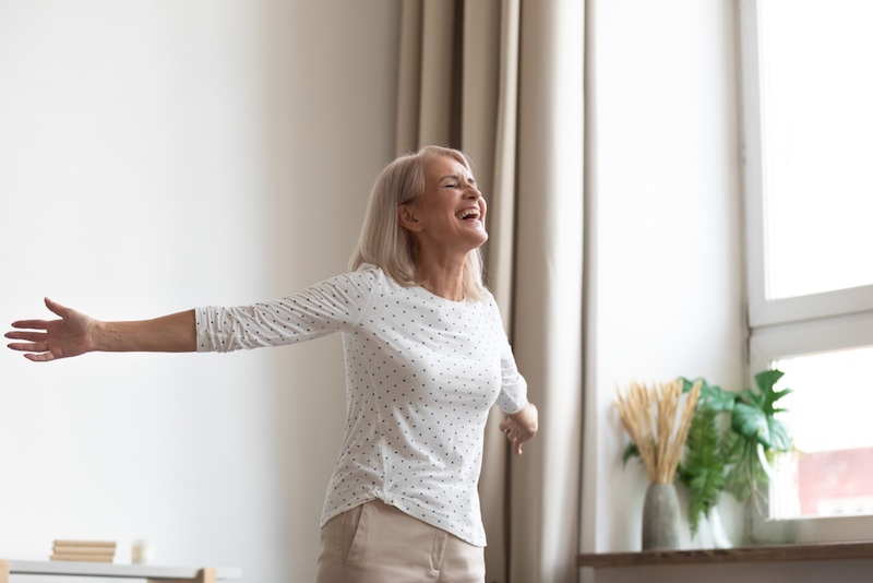 Laughing carefree middle-aged woman standing in living room stretched hands closed eyes breathing fresh air feels happy healthy, starts new day positive mood and thoughts, dancing enjoy life concept | Amazing Benefits Of Turning 50