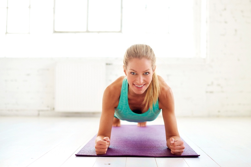 Portrait shot of attractive middle aged woman doing plank exercises on yoga mat in the fitness studio. | turning 50