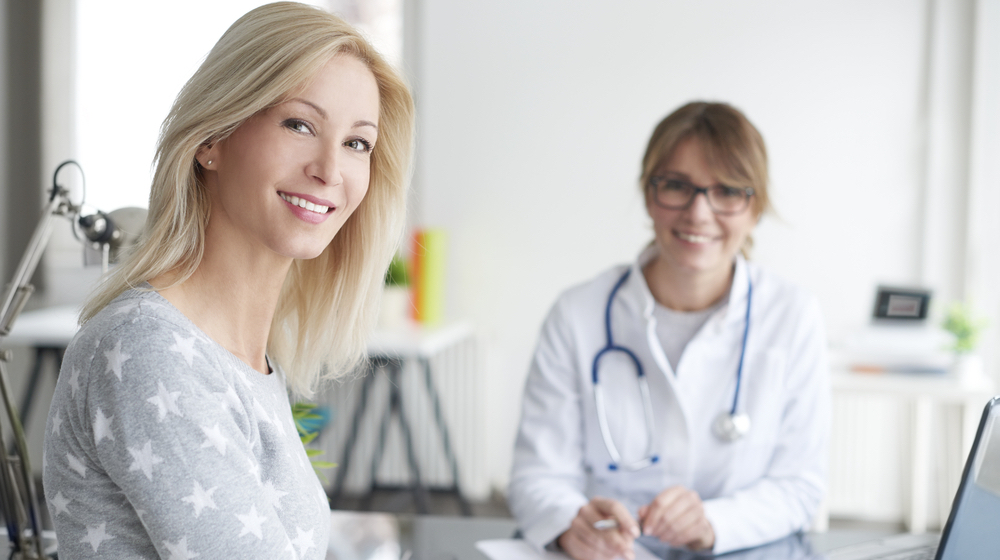 Shot of a beautiful mature woman sitting in doctor's office and consulting with female doctor. | Preventive Care Tests You Need at Ages 50+ | Featured