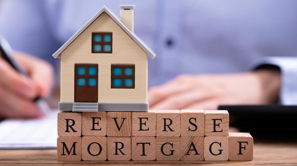 House Model Over Reverse Mortgage Blocks In Front Of Businessman Writing | Will a Reverse Mortgage Work For You? | Featured