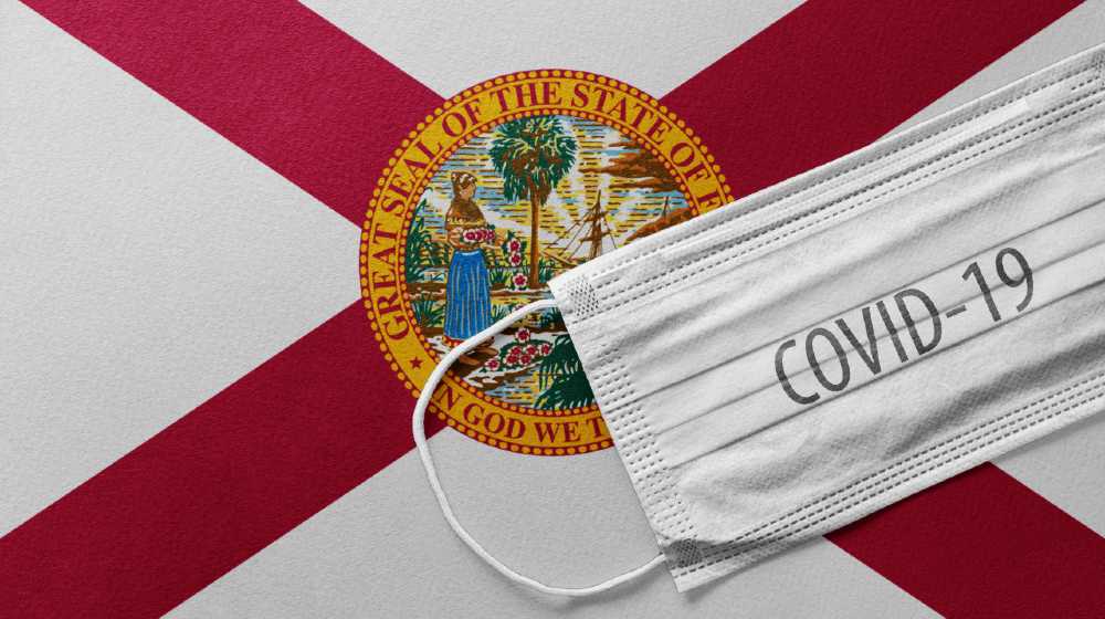 An individual face medical surgical mask on Florida State Flag Background | Florida Posts Record 21,683 COVID Daily Cases | featured
