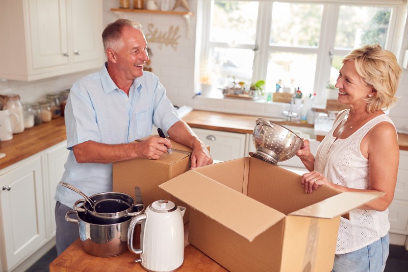 Senior Couple Downsizing In Retirement Packing And Labelling Boxes-Baby Boomers