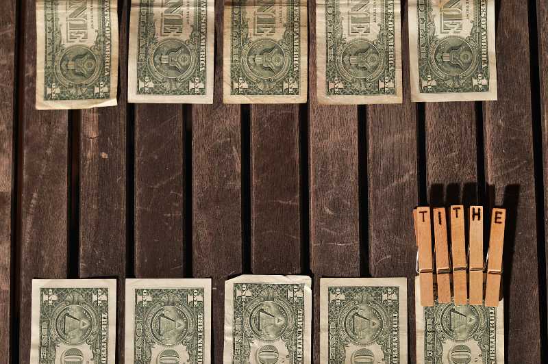 Ten dollar bills on a table and clips with the letters TITHE burned into them on one of the bills-COVID Immunity