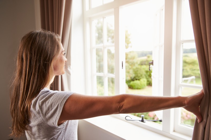 Woman Standing By Bedroom Window And Opening Curtains-Delta Variant