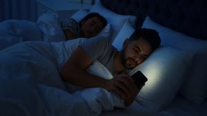 Young man using phone while wife sleeps | Revenge sleep procrastination | Featured