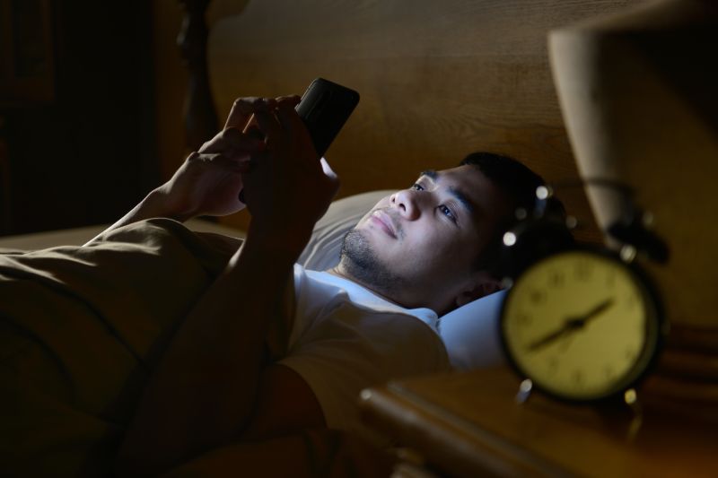 Young man using smartphone bed | Revenge sleep procrastination