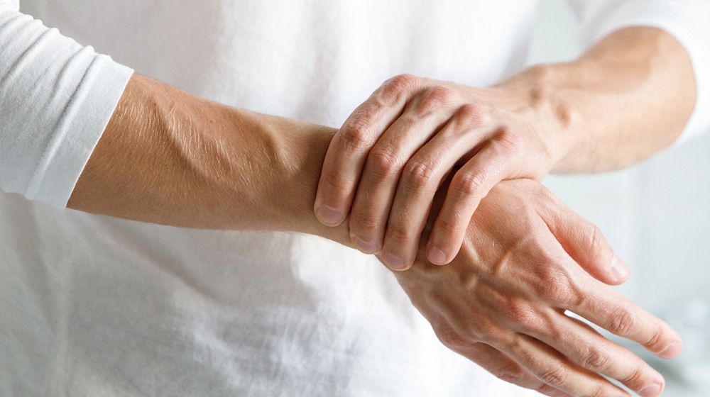 closeup male arms holding his painful | ow to Fix Wrist Pain for Good | Featured