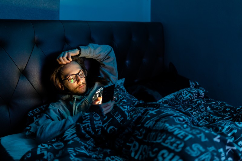 A young man addicted to social media checking his phone before going to bed-Nighttime Routine