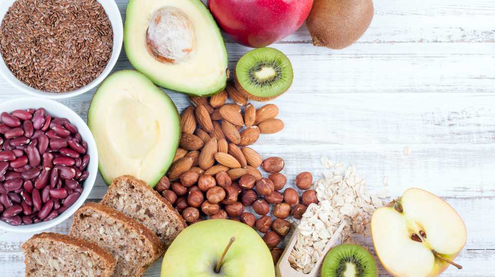 Avocado, flax seeds, whole grain bread, kiwi fruit, nuts, oatmeal, beans and apples on wooden boards | Daniel Diet | What Can You Eat on The Daniel Fast | featured