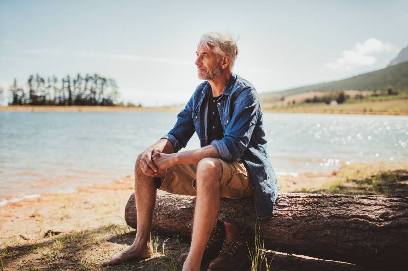 Portrait of a mature man sitting on a log near the lake-Why Camping Is Good For Your Health