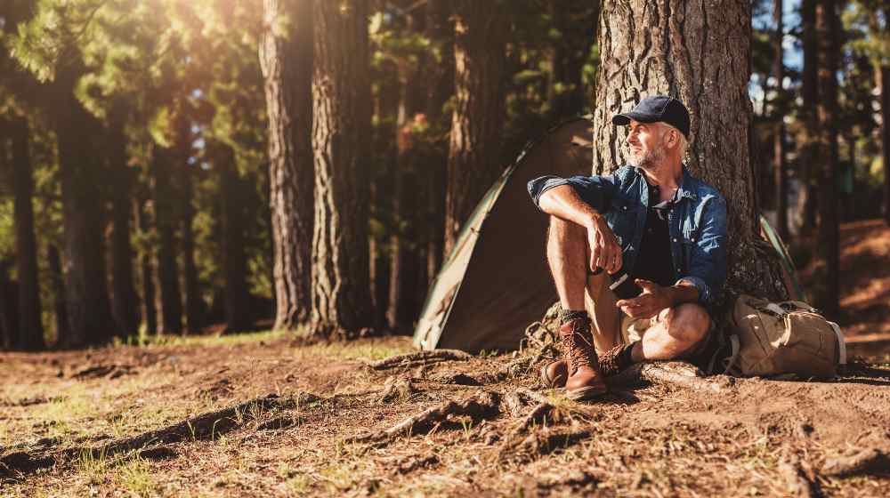 Portrait of senior man sitting by a tree with a tent in background | 5 Reasons Why Camping Is Good For Your Health | featured