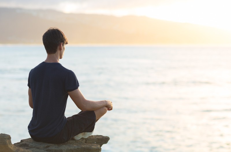 Young man meditating on top ocean cliff during sunset-Circadian Meditation