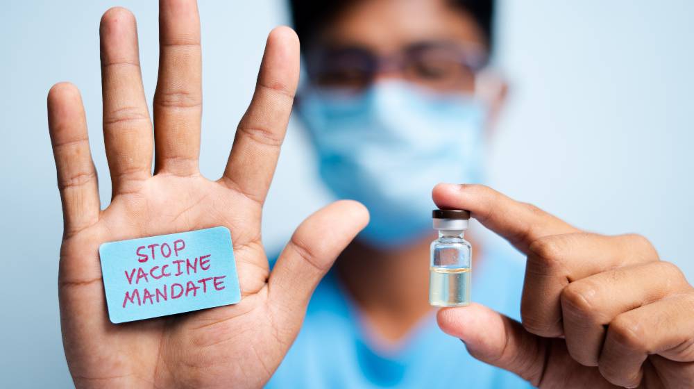 Young man with medical face mask showing stop vaccine mandate | Federal Judge Halts Biden’s Vaccine Mandates In 10 US States | featured