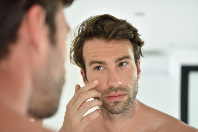 Handsome man applying facial cream in front of mirror | curcumin benefits