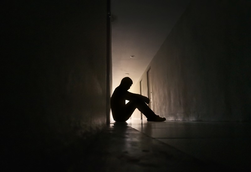 Silhouette of depressed man sitting on walkway of residence building | curcumin benefits