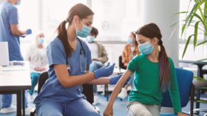 Doctor vaccinating child at clinic. Little girl getting flu shot | No Evidence That Healthy Kids and Adolescents Need COVID Booster Shots, Says WHO | featured
