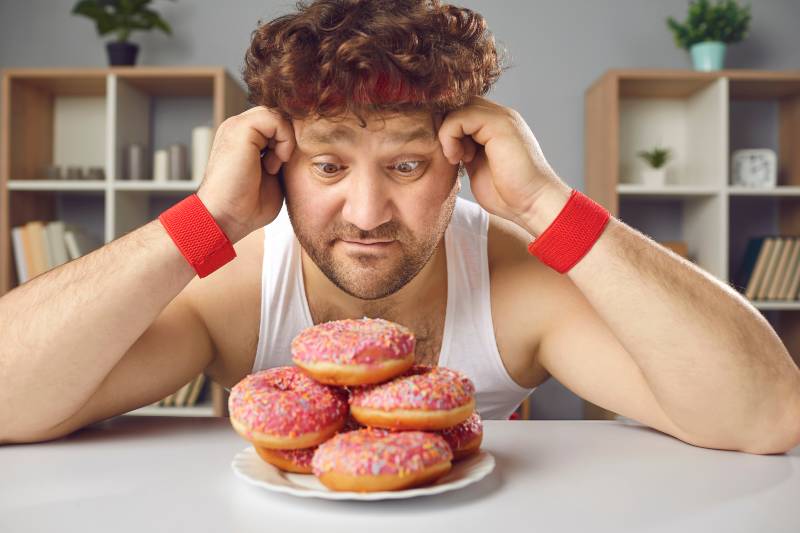Funny athlete tempted by delicious doughnuts forgets about sports workout | do carbs make you fat