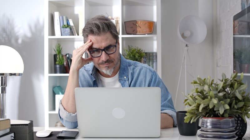 Older man working online with laptop computer at home sitting at desk | Healthy Life Balance