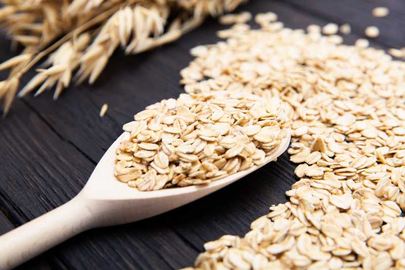 Rolled oats or oat flakes on wooden spoon on dark wooden background with texture | Beta-Glucan