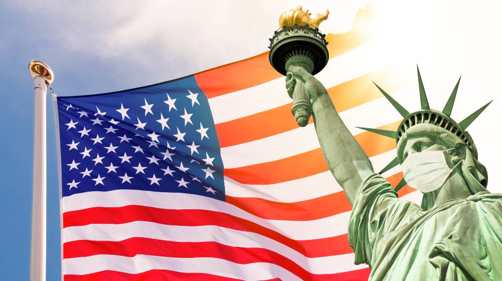 Statue of Liberty wearing a surgical mask, US american flag background | US Sets New Global Daily Record of 1 Million COVID Cases On January 3 | featured