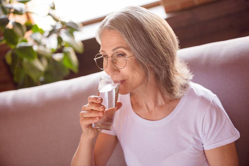 happy adorable retired woman dressed white t-shirt sitting couch drinking water | Stay Hydrated | How to Reverse Prediabetes Naturally