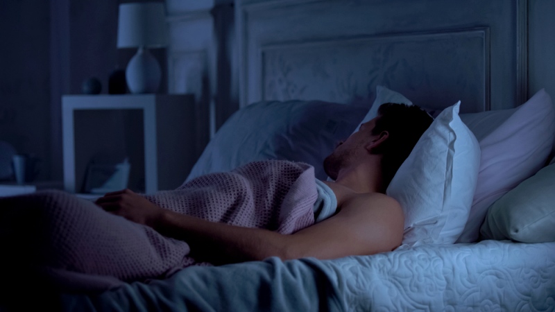 man deeply sleeping on bed dark | how to burn fat while sleeping