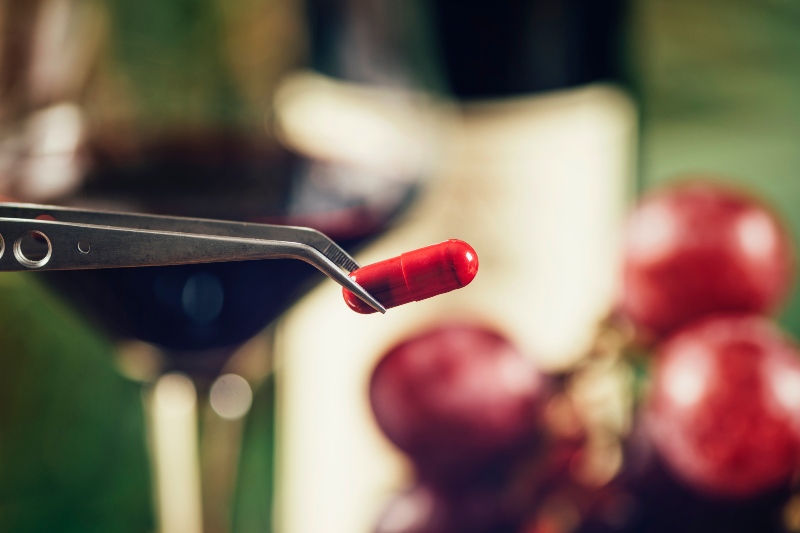 Resveratrol Supplements with Blurred Grapes and Glass of Red Wine in Background | How to Increase Insulin Sensitivity Naturally
