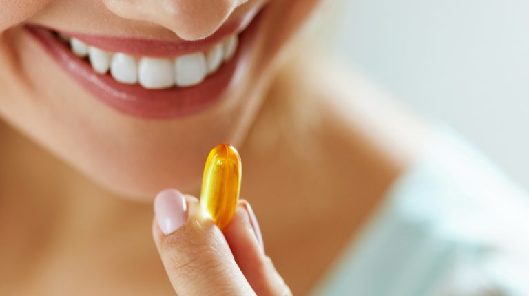 vitamin supplement closeup beautiful young woman | Which Essential Fatty Acid Is Responsible for Lowering the Risk of Coronary Heart Disease? | Featured