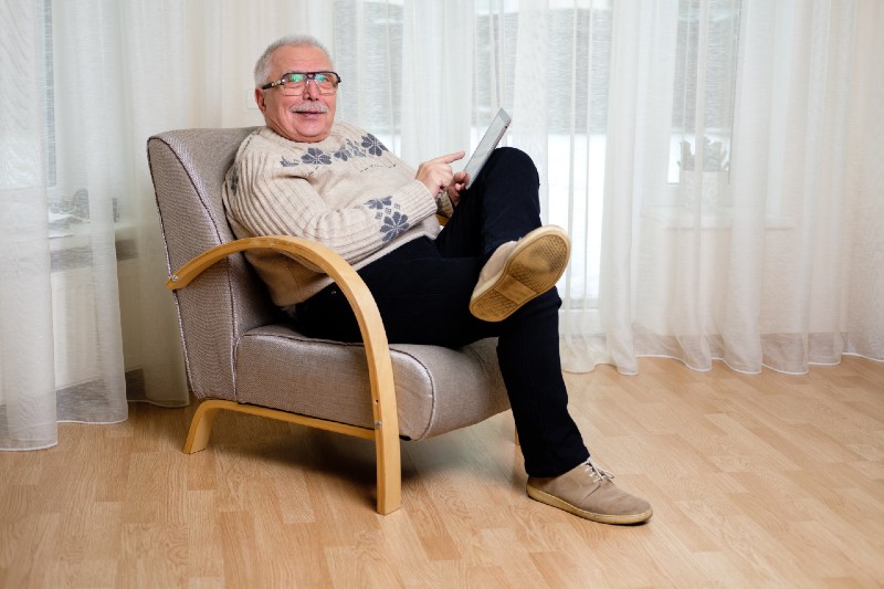 Happy and successful senior male 65-75 years old with tablet pc computer sitting in armchair at home | Lowering Your Income