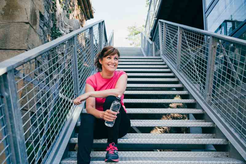 Happy and beautiful middle aged woman sitting on metallic stairs | 5 Nutrition Principles For Healthy Weight And High Performance