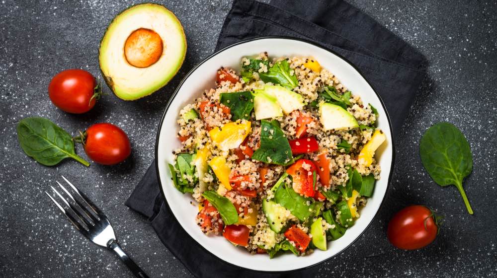 Quinoa Benefits - Easy to Incorporate to Diet _ Quinoa salad with spinach, avocado, paprika and tomatoes on black stone table